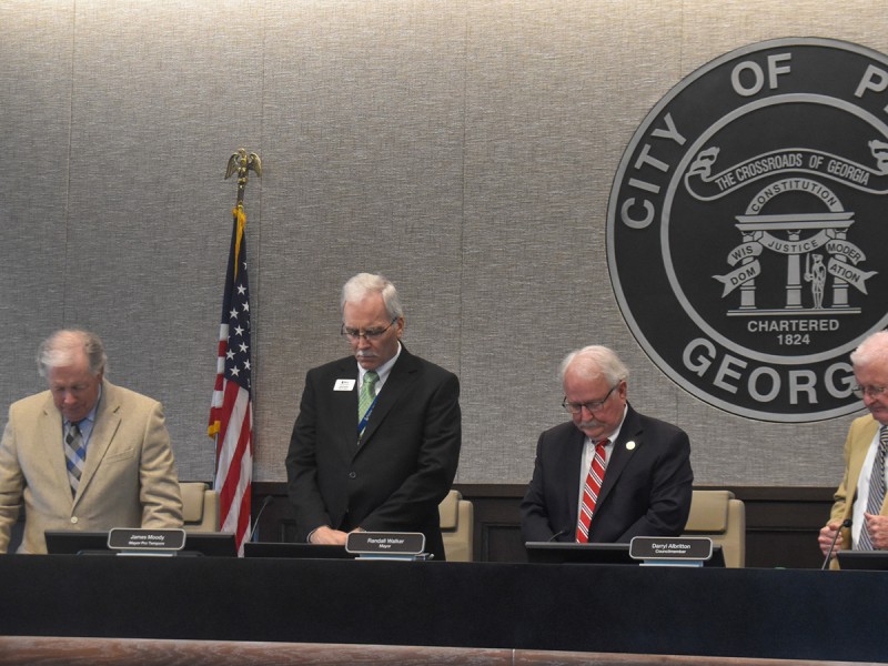 Four men in suits standing with their heads down. They are doing a moment of silence.